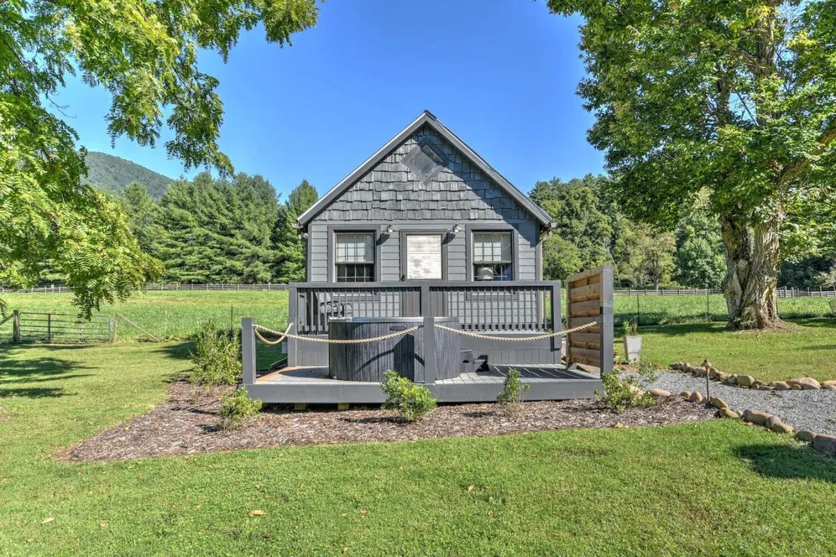 The exterior of a peaceful gray house features a well-maintained deck set against a dramatic mountain backdrop. The surrounding greenery and open skies invite guests to unwind outdoors, watch sunsets, and bask in the area’s natural splendor.