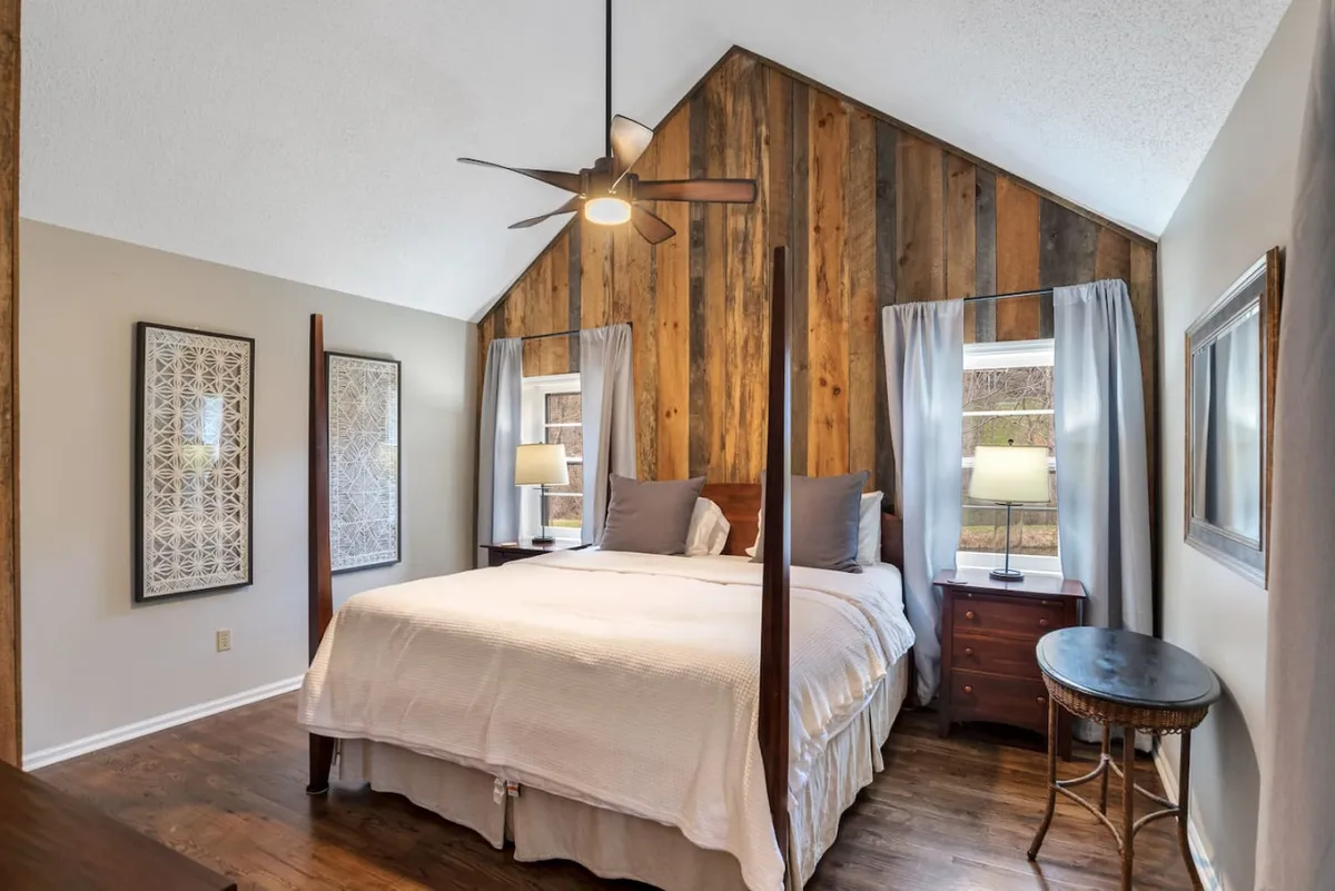 A serene bedroom featuring a four-poster bed with plush linens, a wooden accent wall, and nightstands with soft lighting and decorative artwork. The ambiance is tranquil, inviting relaxation and restful sleep.