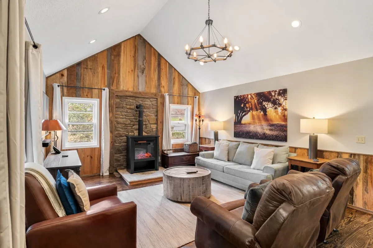A warm, inviting interior with a rustic stone fireplace, wooden walls, cozy sofa seating, and decorative touches. The glow of the fire and soft lighting create a welcoming space ideal for gathering after a day outdoors.