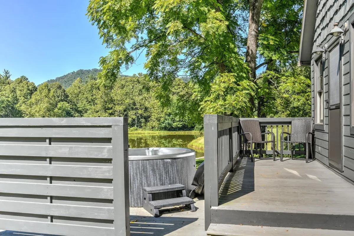 A serene exterior shot featuring a hot tub set on a deck overlooking tranquil water, with surrounding trees providing lush greenery. The inviting hot tub is positioned to enjoy the sunset and offers a clear visual connection between relaxation and natural beauty.